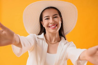 Sarı arka planda selfie çeken yaz şapkalı şık genç kadın, yakın plan.