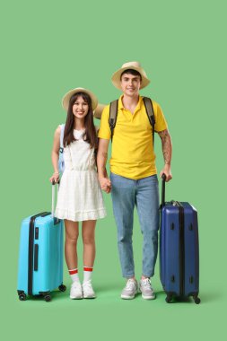 Yeşil arka planda el ele tutuşan bavullu iki turist.