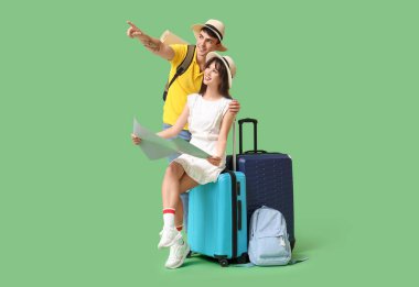 Birkaç turist harita ve bavullarıyla yeşil arka plandaki bir şeyi işaret ediyor.