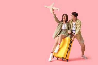 Pembe arka planda bavul ve kağıt uçakla birkaç turist.