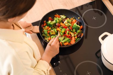 Mutfakta kaşık kaşık sebze kızartan bir kadın.