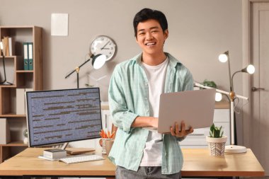 Erkek Asyalı programcı ofiste dizüstü bilgisayarla çalışıyor.