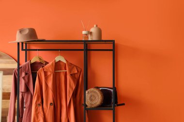 Koridordaki turuncu duvarın yanında palto, çanta ve şapkayla dizilin.