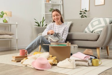 Evde bağışta bulunmak için ayakkabılarını kutuya koyan genç bir kadın.