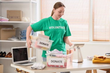 Merkezde tablet bilgisayar kullanan bağış için konteynır taşıyan gönüllü bir kadın.