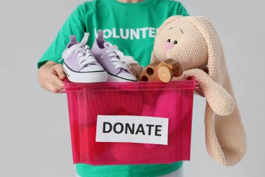 Hafif arka planda bağışlanmak üzere giysi ve oyuncak konteynırına sahip kadın gönüllü, yakın plan