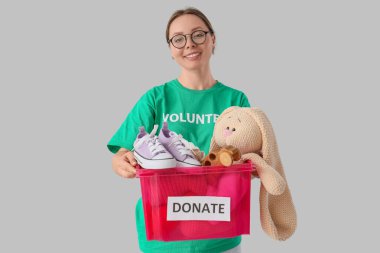 Hafif arka planda bağışlanmak üzere giysi ve oyuncak konteynırıyla gönüllü bir kadın.