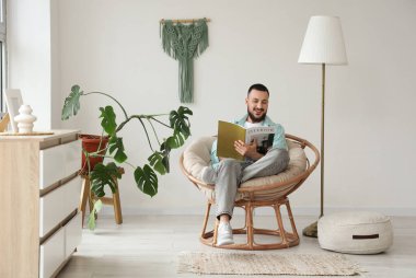 Evde kozalı sandalyede kitap okuyan yakışıklı bir adam.