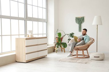 Evde kozalı sandalyede kitap okuyan yakışıklı bir adam.