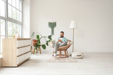 Evde kozalı sandalyede cep telefonu kullanan yakışıklı adam.