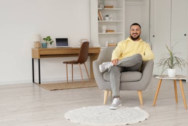 Evdeki gri koltukta oturan yakışıklı adam.