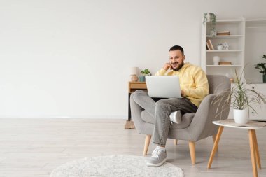 Evdeki gri koltukta dizüstü bilgisayar kullanan yakışıklı adam.