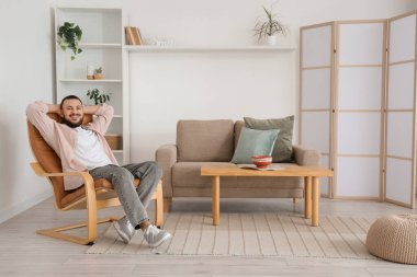 Evdeki kahverengi koltukta oturan yakışıklı adam.