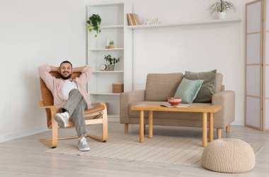 Evdeki kahverengi koltukta oturan yakışıklı adam.