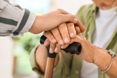 Evde sopayla el ele tutuşan genç kadın ve büyükanne, yakın çekim. Bakım kavramı