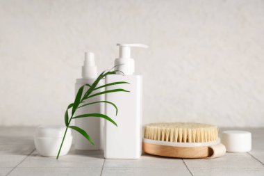 Beyaz fayans üzerinde kozmetik ürünler ve palmiye yaprağı ile selülit önleyici masaj fırçası