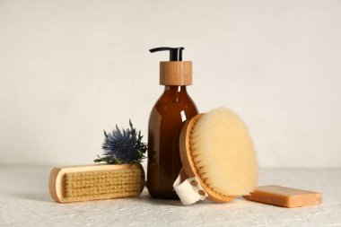 Beyaz grunge masasında bir şişe krema ve çiçekli selülit önleyici masaj fırçaları.