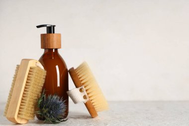 Beyaz grunge masasında bir şişe krema ve çiçekli selülit önleyici masaj fırçaları.