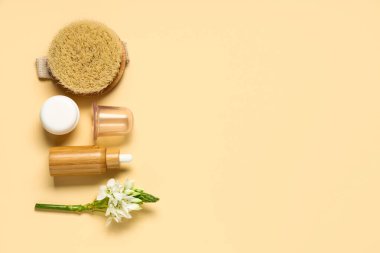Antiselülit masajı için fırçalı süpürge kavanozu, kozmetik ürünler ve bej arka planda çiçek.