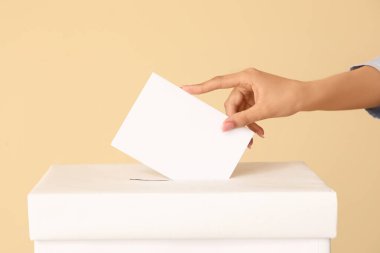 Kadın el, oy pusulasına bej arka planda oy veriyor.