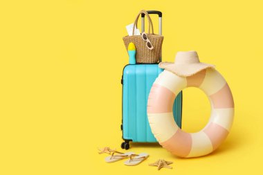 Çanta, şişme yüzük, güneş kremi şişesi ve sarı arka planda plaj aksesuarları.