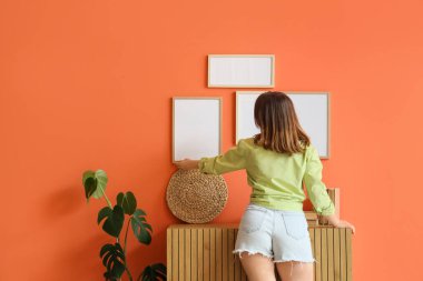 Evdeki turuncu duvara boş çerçeveler asan genç bir kadın.