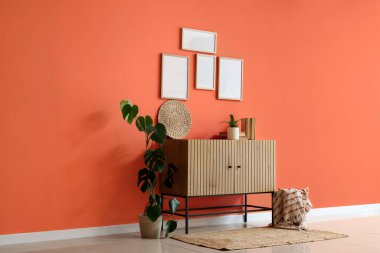 Sandıkta kitaplar, bitkiler ve turuncu duvardaki boş çerçeveler.