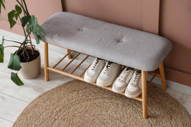 Koridordaki kahverengi duvarın yanındaki yumuşak bankta ayakkabılar ve palmiye bitkisi.