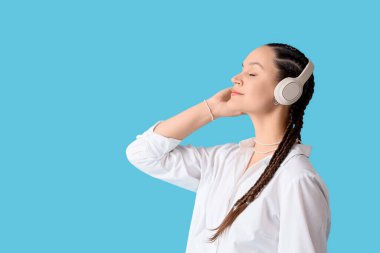 Mavi arka planda rastalı ve kulaklıklı genç bir kadın.