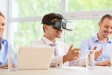 Genç işadamı ofisinde iş arkadaşlarıyla VR gözlükleri kullanıyor.