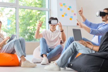 Ofisteki puf minderlere VR gözlüğü takan genç meslektaşlar.
