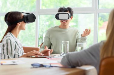 Ofisteki masada VR gözlüğü kullanan genç meslektaşlar.