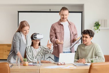 Ofisteki meslektaşlarıyla VR gözlüğü takan genç bir kadın.