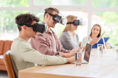 Bilgisayarlı genç bir adam ve iş arkadaşları ofiste VR gözlüğü kullanıyorlar.