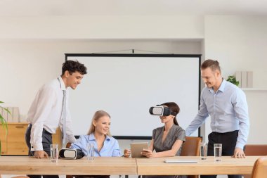 Ofisteki meslektaşlarıyla birlikte VR gözlüğü kullanan genç bir iş kadını.