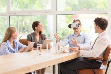 Genç işadamı ofisinde iş arkadaşlarıyla VR gözlükleri kullanıyor.
