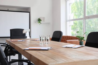 Konferans salonunda yapılacak iş toplantısı için hazırlanmış su ve panolarla dolu bir masa.