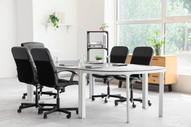 Konferans salonunun içinde masa, raf ünitesi ve bitkiler var.