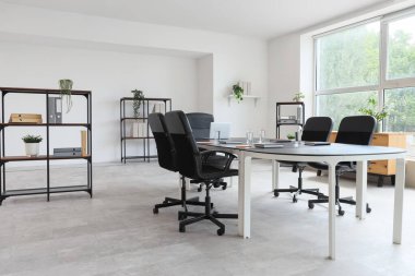 Konferans salonunun içinde masa, bitki ve raf üniteleri var.