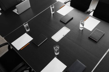 Konferans salonunda yapılacak iş toplantısı için hazırlanmış su ve kağıt kağıtlarla dolu bir masa.