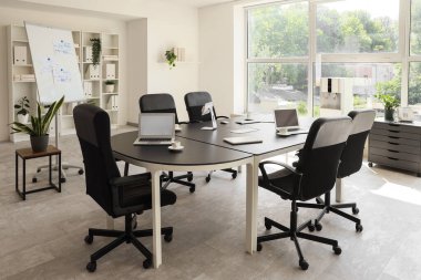 Konferans salonunun içinde masa, çizelge ve bitkiler var.