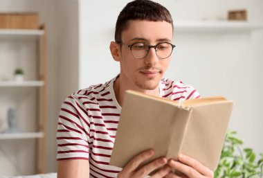 Gözlüklü genç adam evde kitap okuyor, yakın plan.