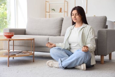 Evdeki halıda meditasyon yapan güzel genç bir kadın.