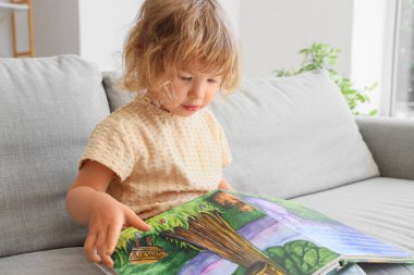 Evdeki kanepede kitap okuyan tatlı küçük kız.