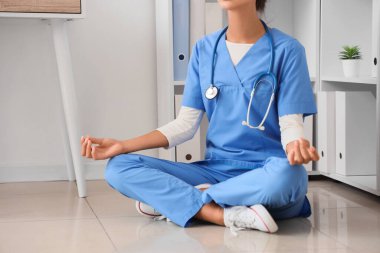 Kadın doktor klinikte yerde meditasyon yapıyor.