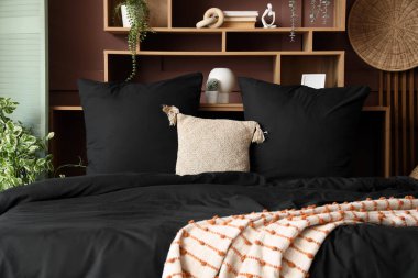 İçinde siyah keten, raf ve bitkiler olan şık bir yatak odası.