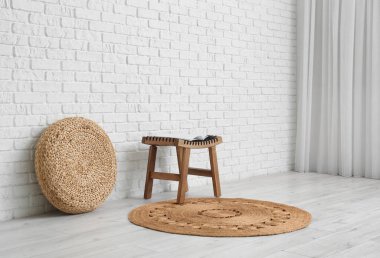 Beyaz tuğla duvarın yanında puf ve hasır halılı bir masa.