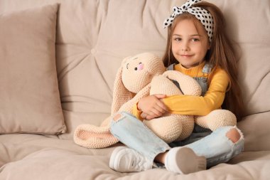 Evdeki kanepede oyuncak tavşancığı olan sevimli küçük kız.