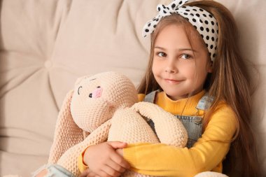 Evdeki kanepede oturan oyuncak tavşancığı olan sevimli küçük kız.