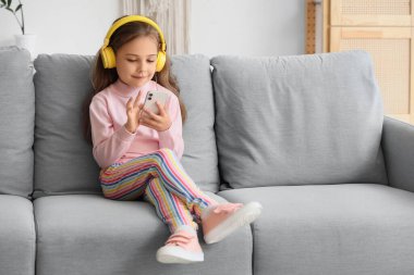 Kulaklık takıp evdeki koltukta cep telefonu kullanan tatlı bir kız.